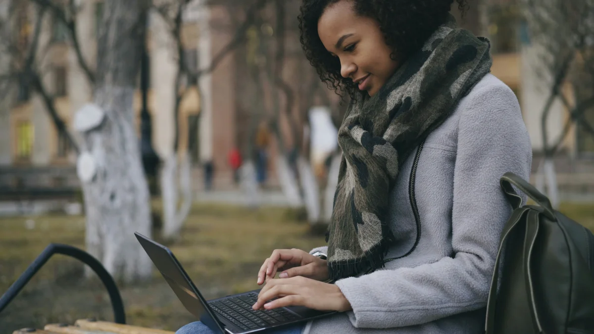 Student smiling while working on a laptop outdoors